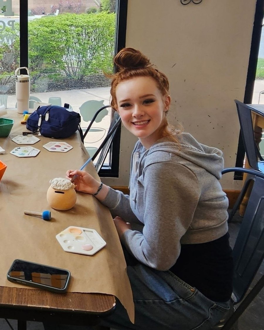 Kamryn Fenn painting a ceramic piece at a paper-covered table with palettes and glaze bowls