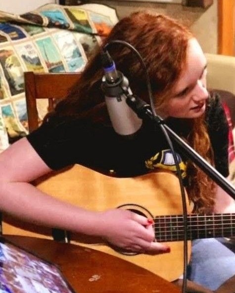 Kamryn Fenn playing acoustic guitar into a microphone at home