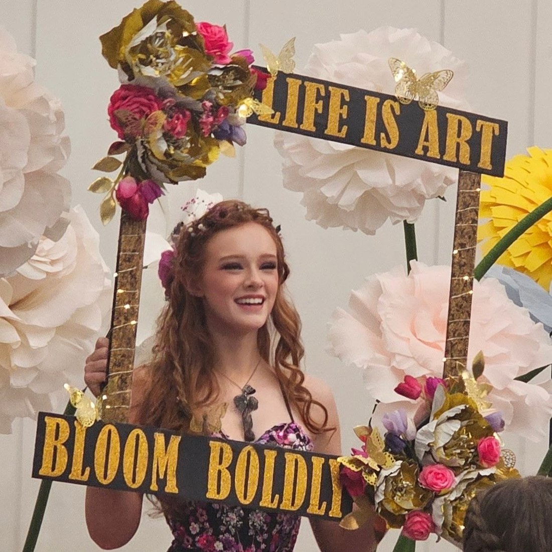Kamryn Fenn on stage holding her lit Life is Art, Bloom Boldly frame